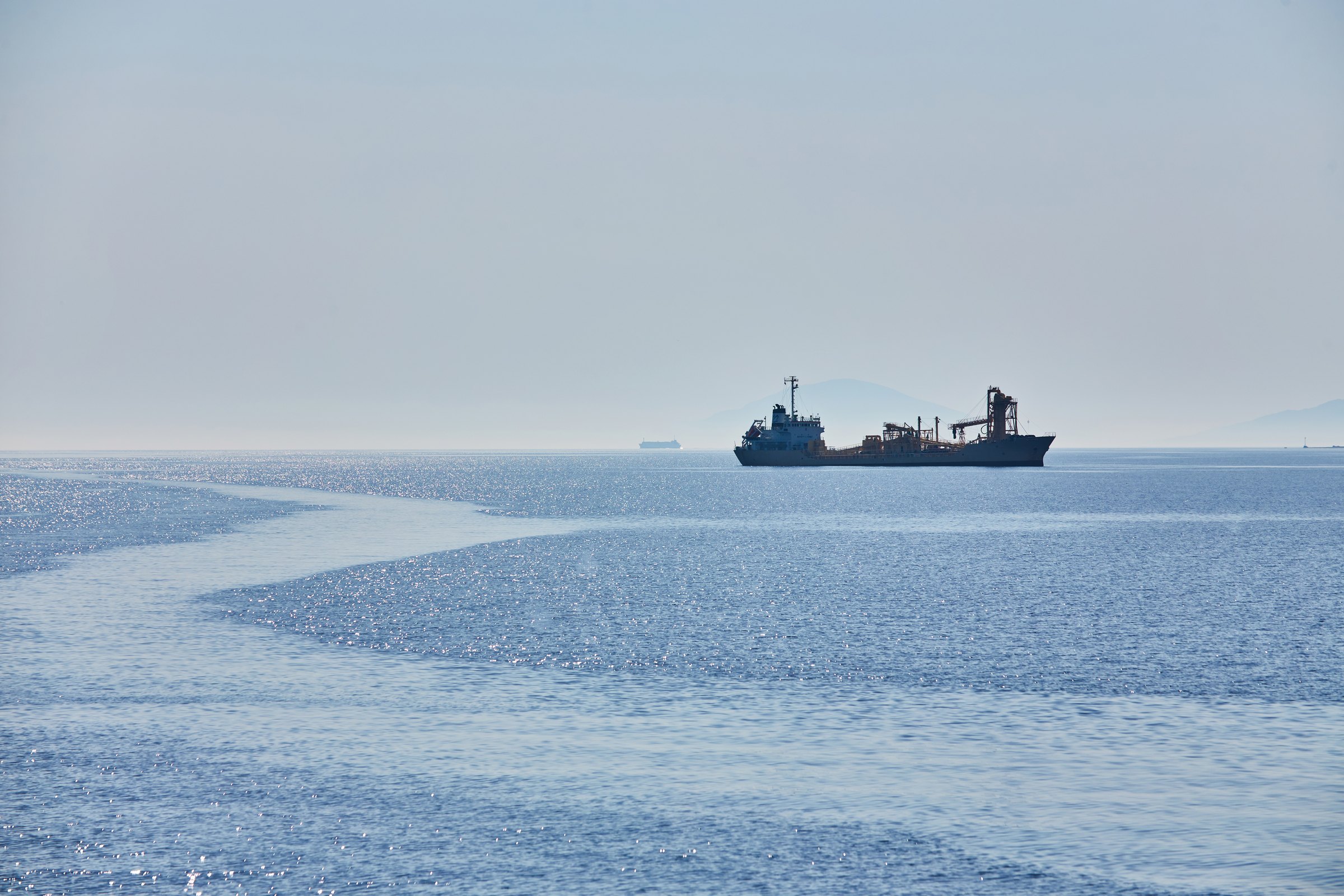 Industrial vessel on a calm, hazy sea far off on the horizon