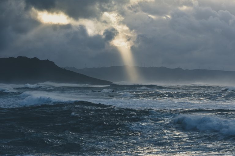 Rough grey sea under dark clouds with a shaft of light breaking through over a distant headland