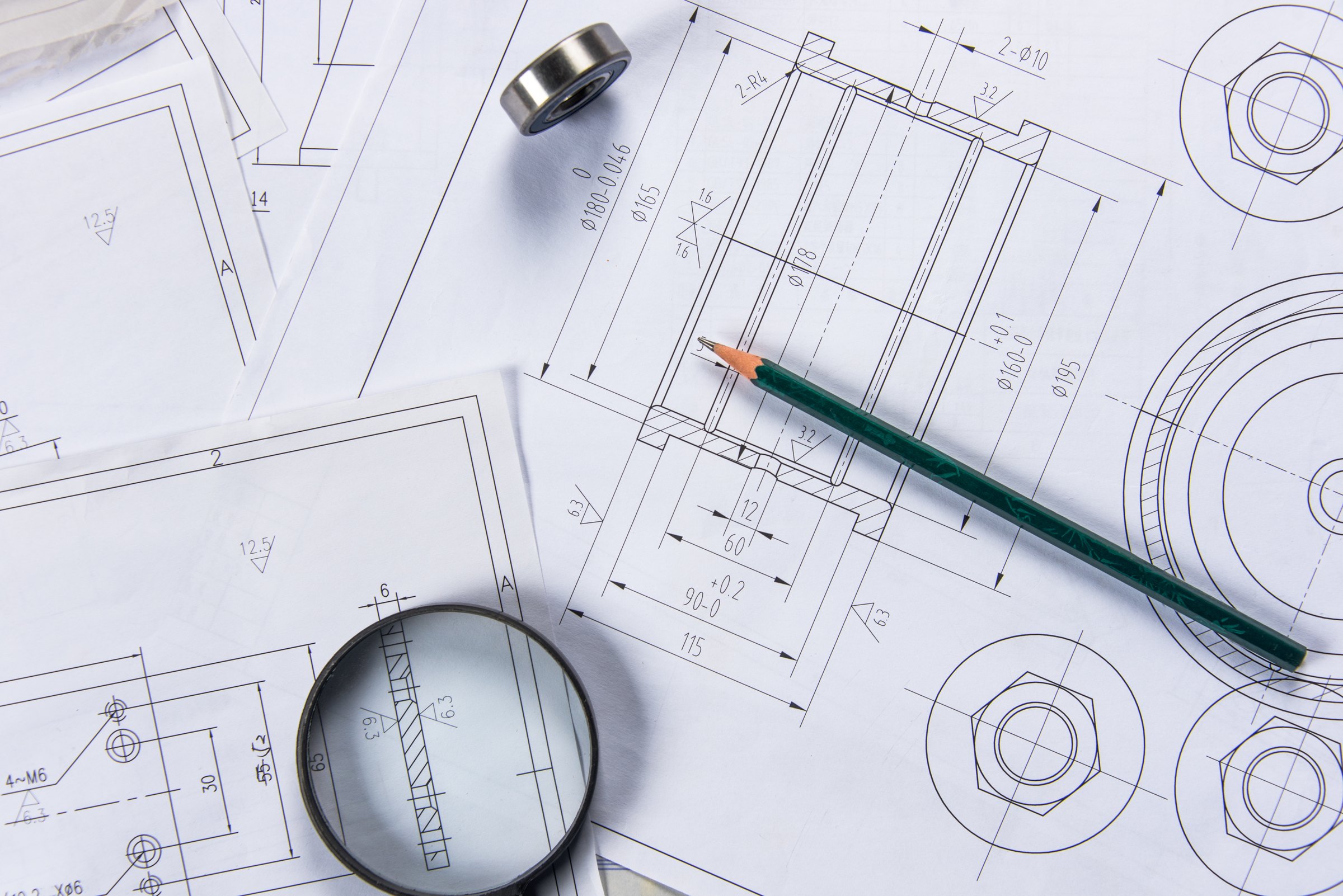 Mechanical engineering drawings with a magnifying glass, a ball bearing and a pencil laid on top