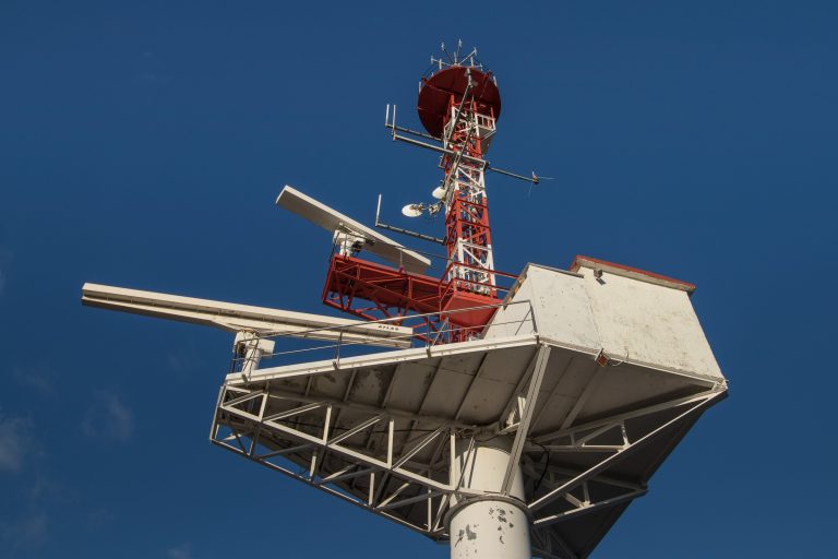 Radar scanners and antennas on a mast platform against a deep blue sky