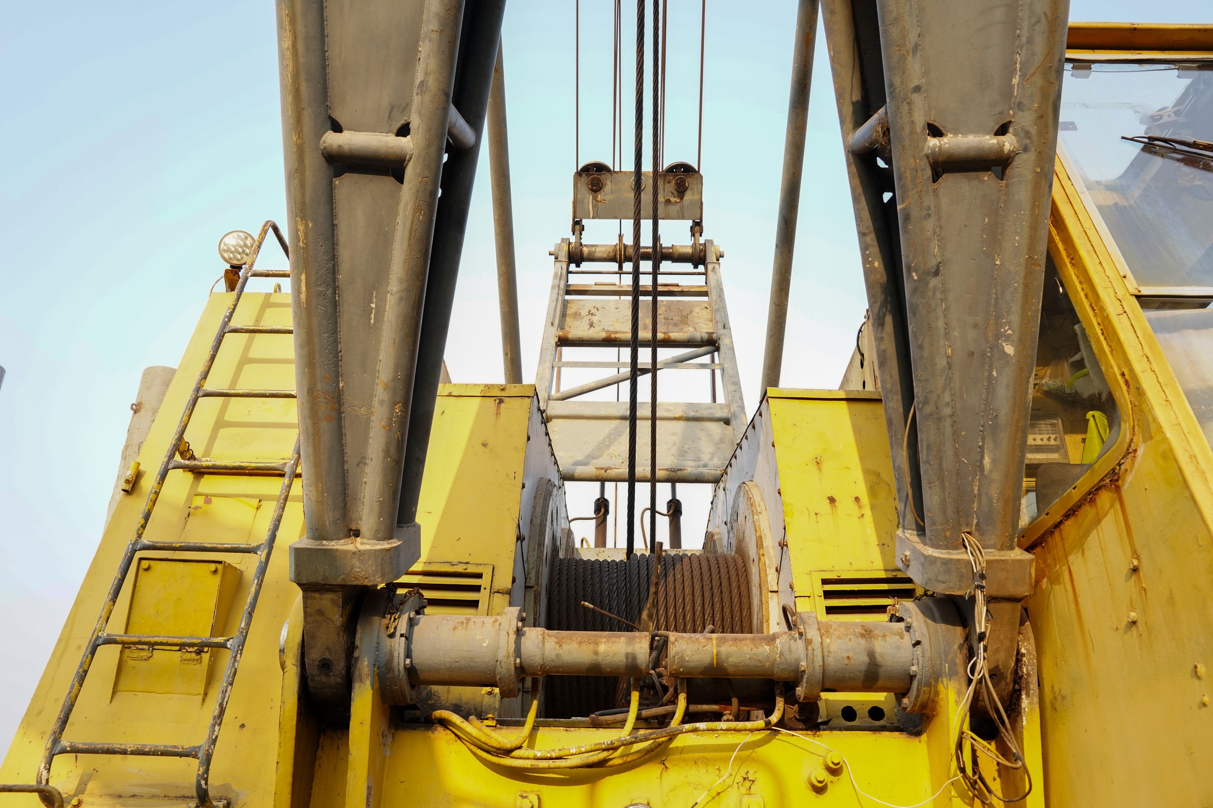 Base of a yellow crane boom with its wire-rope winch drum, sheaves and access ladder