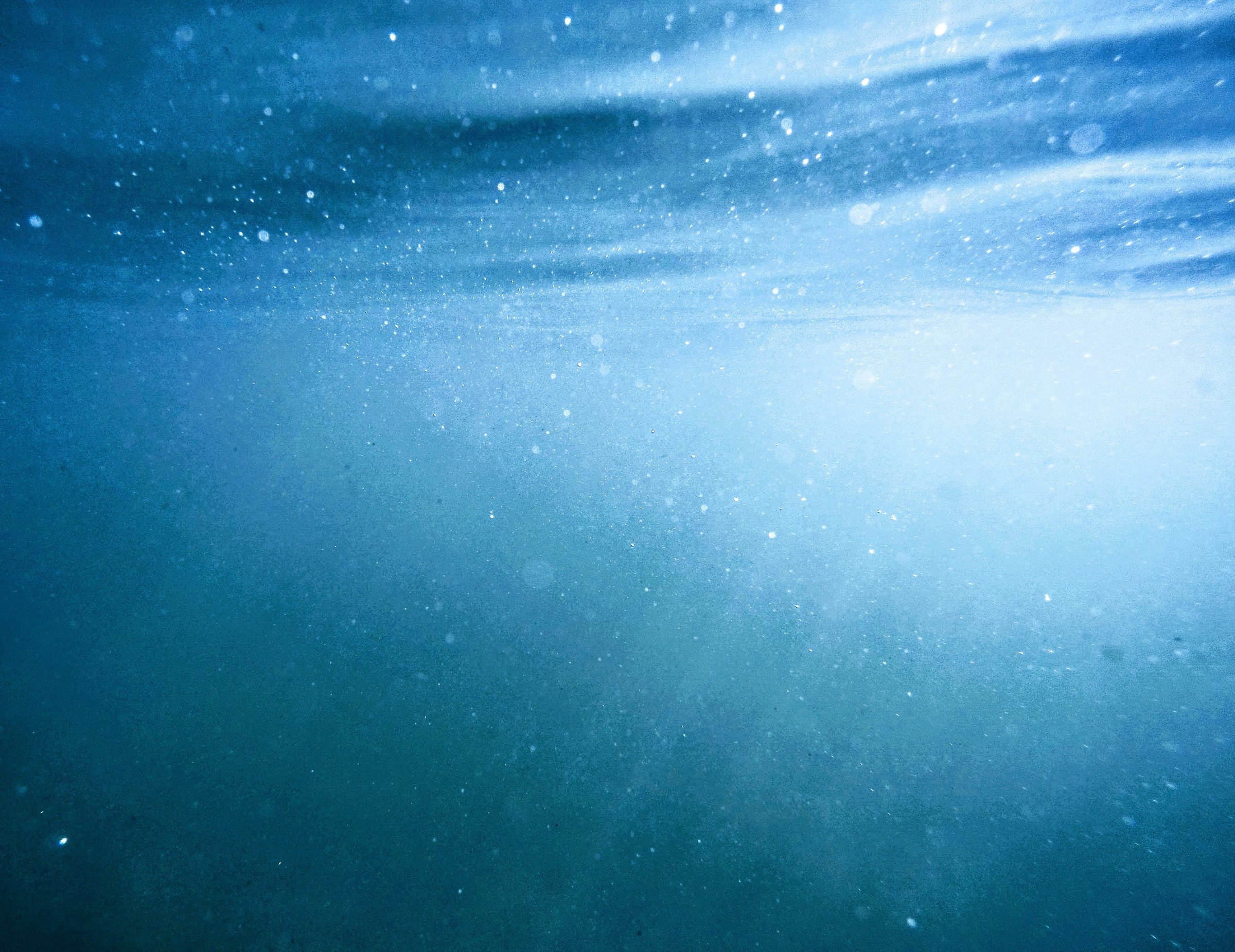 Soft daylight filtering down through blue ocean water seen from below the surface