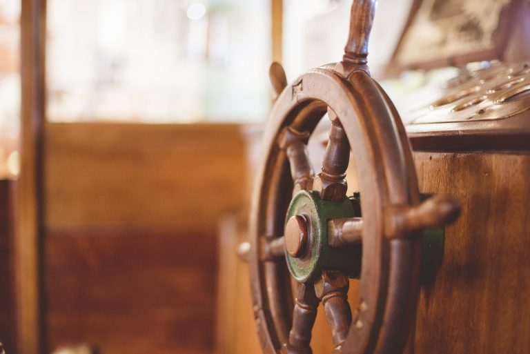 Wooden ship's wheel in a softly lit wheelhouse with a blurred background