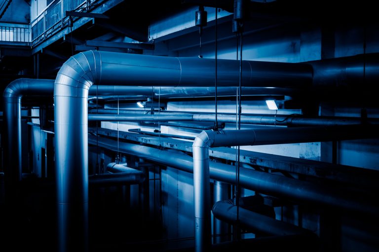 Insulated steel pipework and cable runs in a dimly lit machinery space