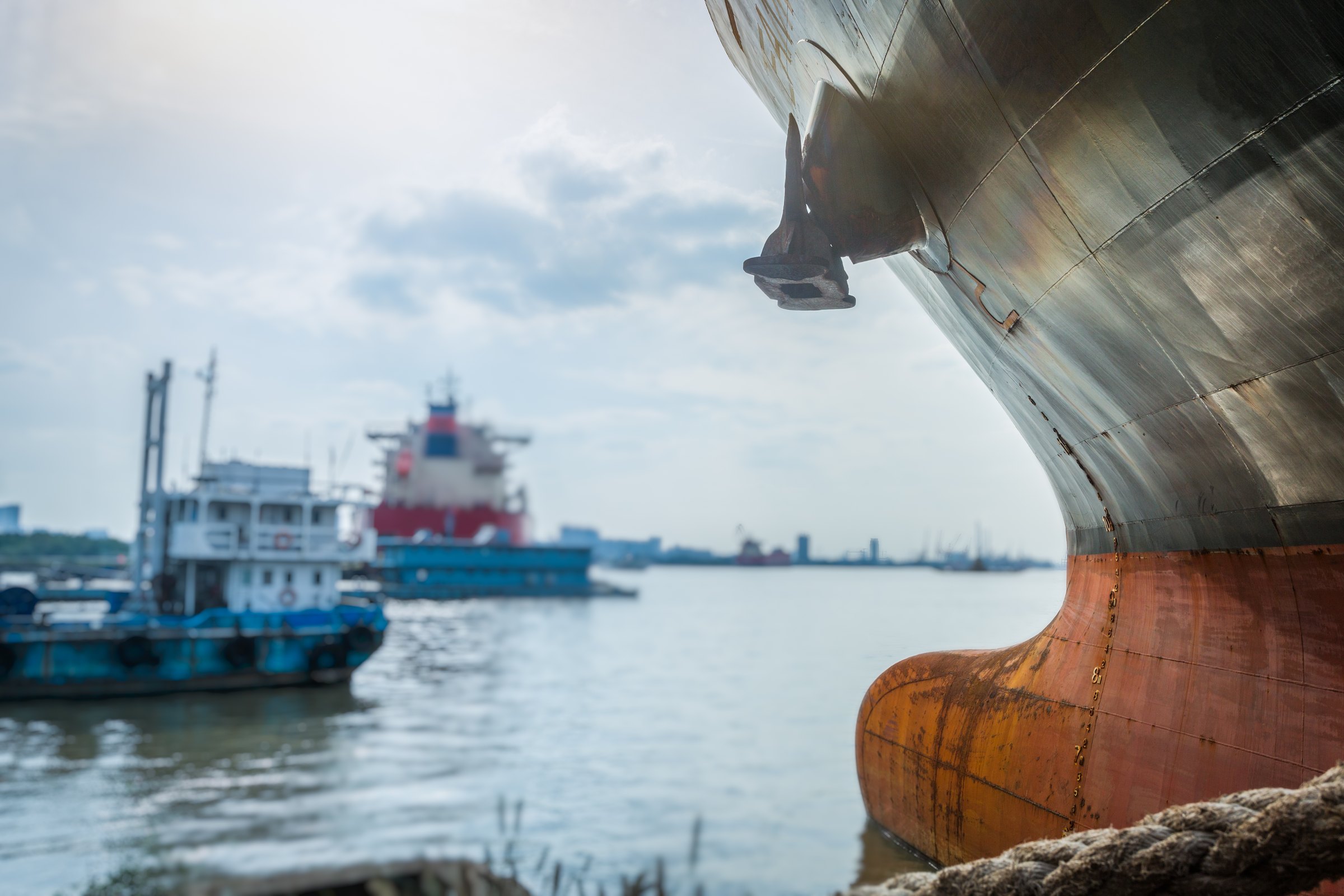 Weathered steel bow of a large merchant ship with rust on the bulbous bow and anchor