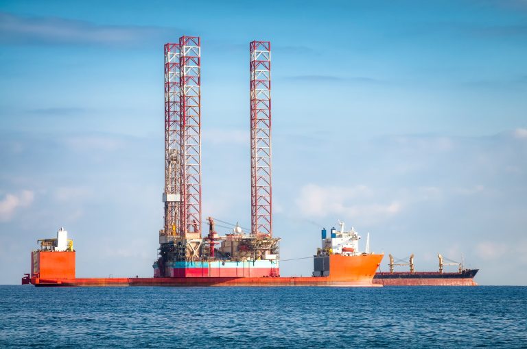 Jack-up rig carried on a semi-submersible heavy-lift vessel at sea under a blue sky