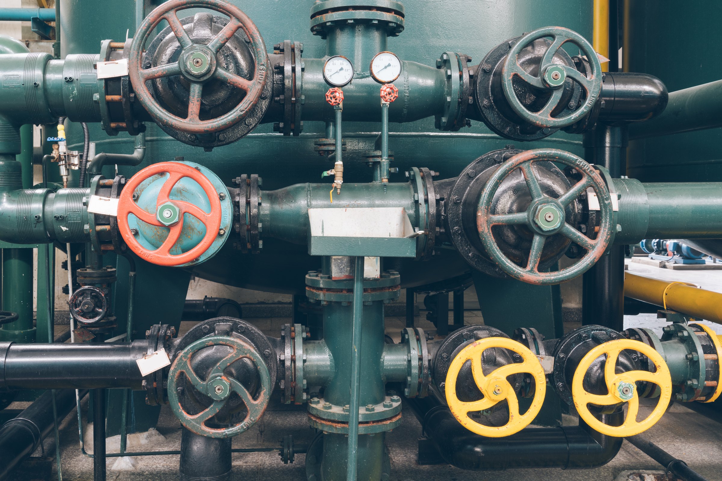 Industrial manifold with several handwheel valves and pressure gauges on dark green pipework