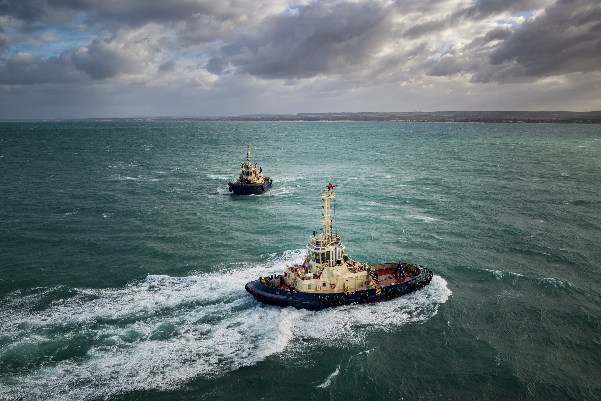 Two tugboats manoeuvring together at sea under a heavy, cloudy sky